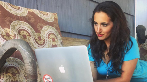 Paula Pant working on her laptop while sitting comfortably on a couch, representing the freedom-focused lifestyle she advocates through the Afford Anything blog.